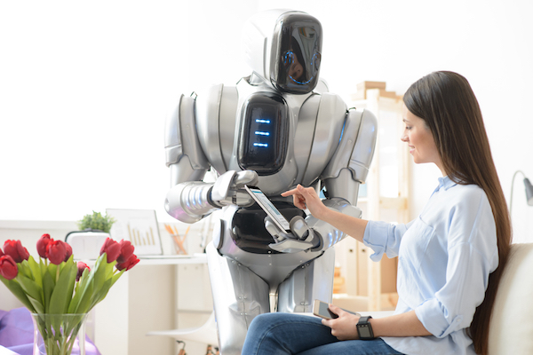 Touch the world. Delighted pretty smiling woman sitting on the couch and using tablet while robot holding it